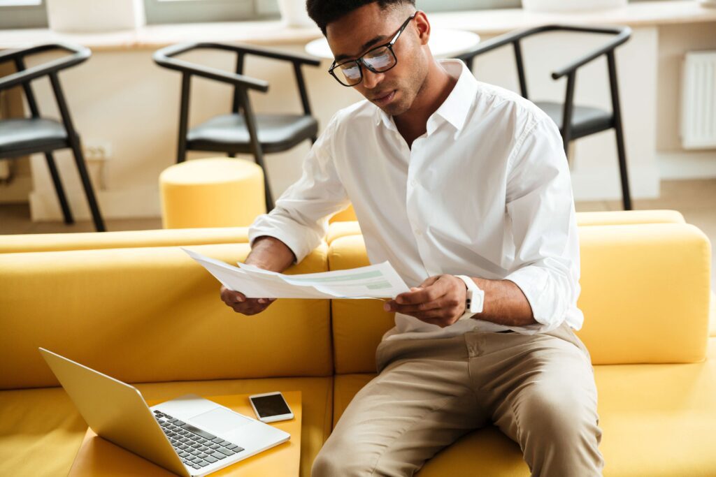 Man reviewing immigration documents on a laptop while checking paperwork related to visa extension status in the U.S.