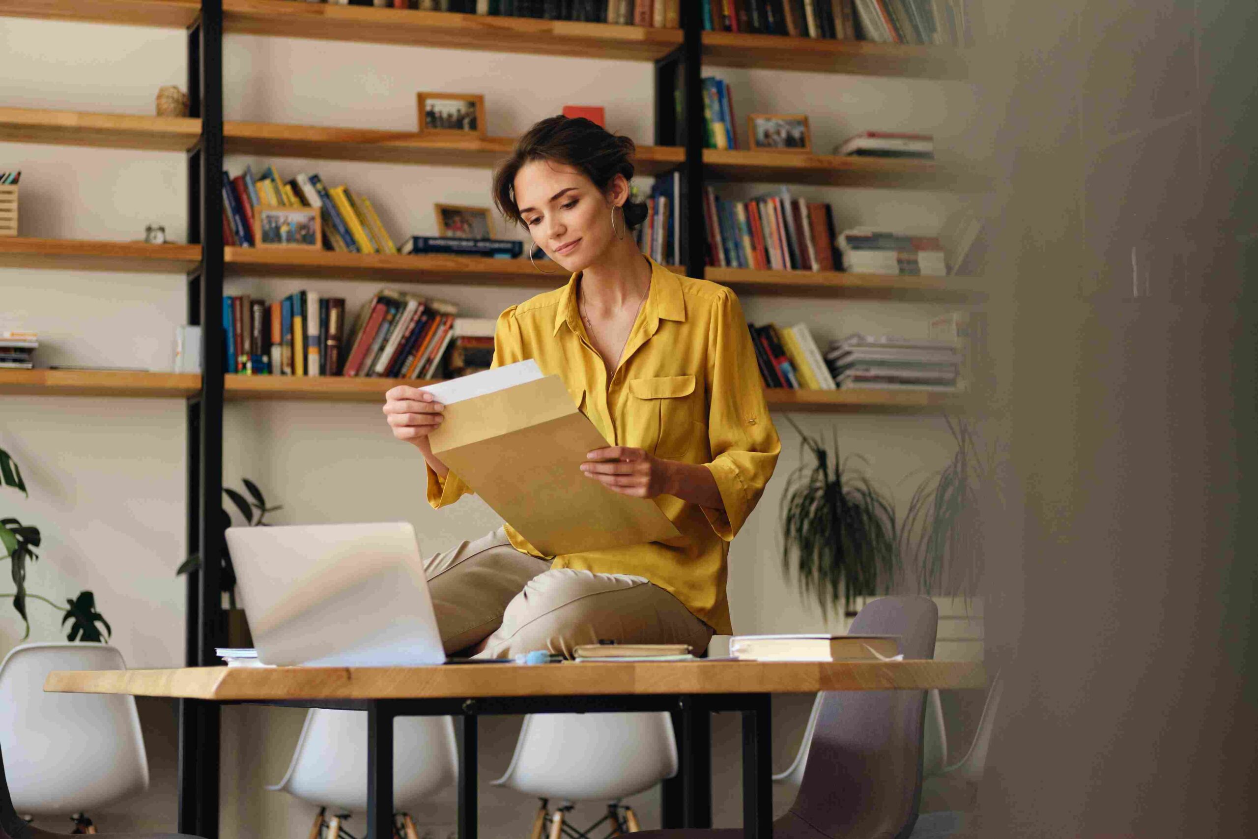 Woman reviewing documents at a desk with a laptop in a modern home office.